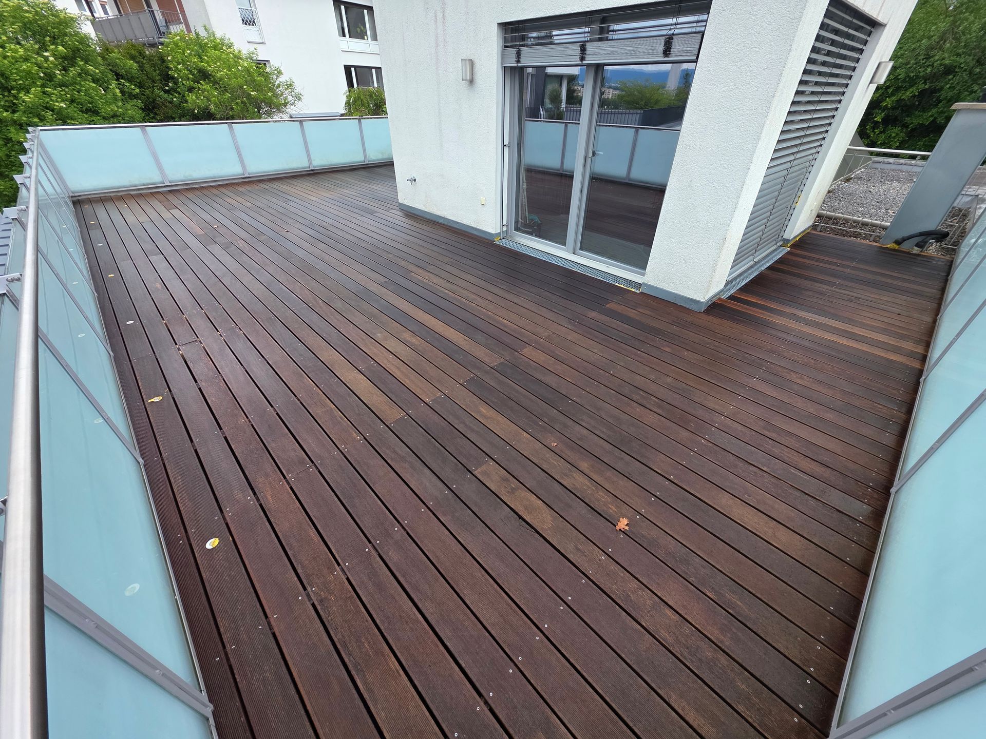 Holzterrasse auf dem Dach mit Glasgeländer und weißen Gebäudewänden, von oben betrachtet.