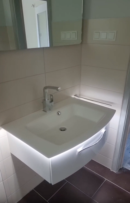 Modernes Badezimmer mit Waschbecken, Spiegel, weißem Waschtisch und beige gefliesten Wänden.