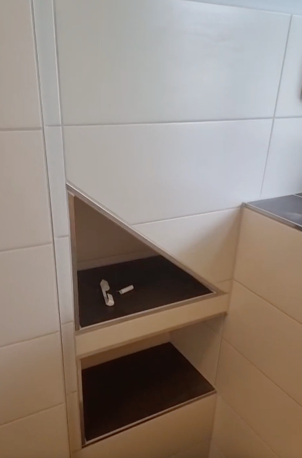 Eckschrank fürs Badezimmer mit zwei offenen Regalböden, in einem davon befindet sich ein kleines Werkzeug.
