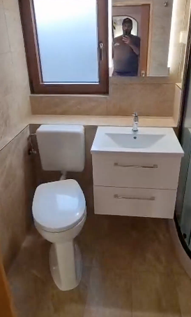 Kleines Badezimmer mit Toilette, weißem Waschtischunterschrank, Spiegel und Holzbodenoptik.