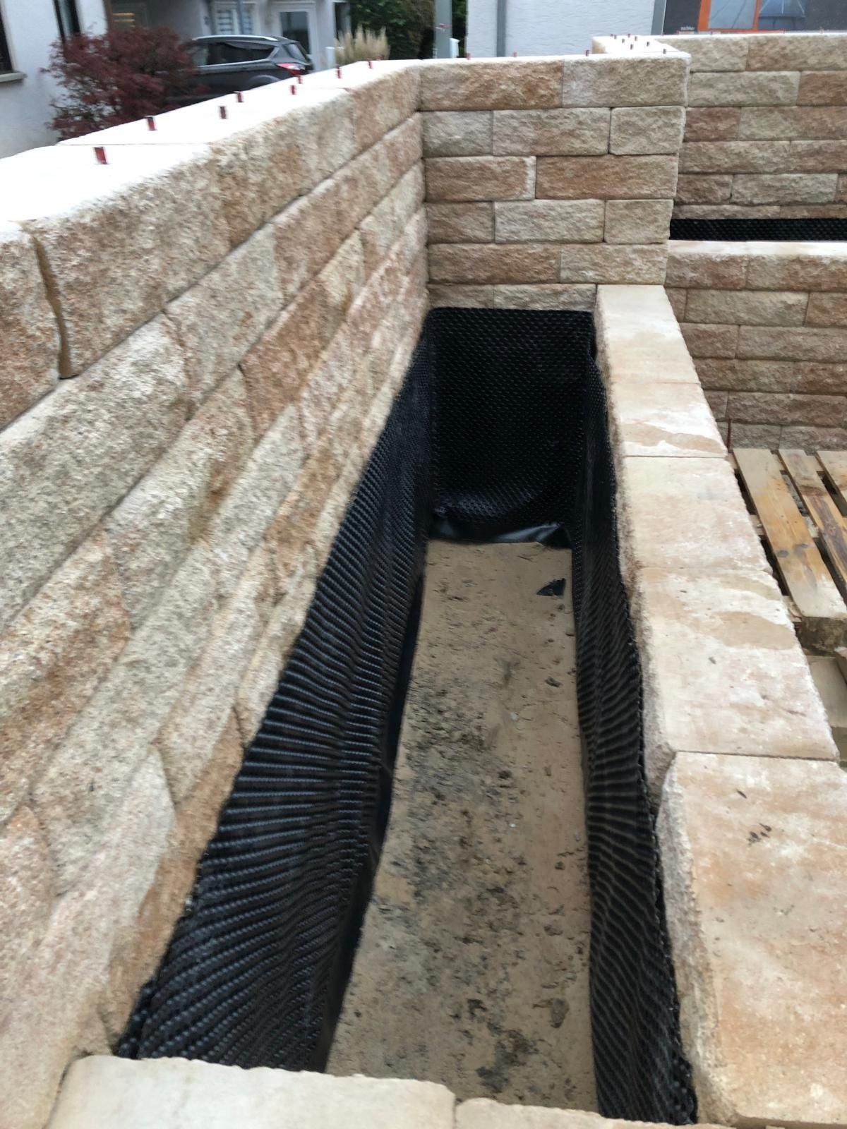 Steinstützmauer um einen schmalen Entwässerungsgraben mit schwarzer Auskleidung und Kiesbett