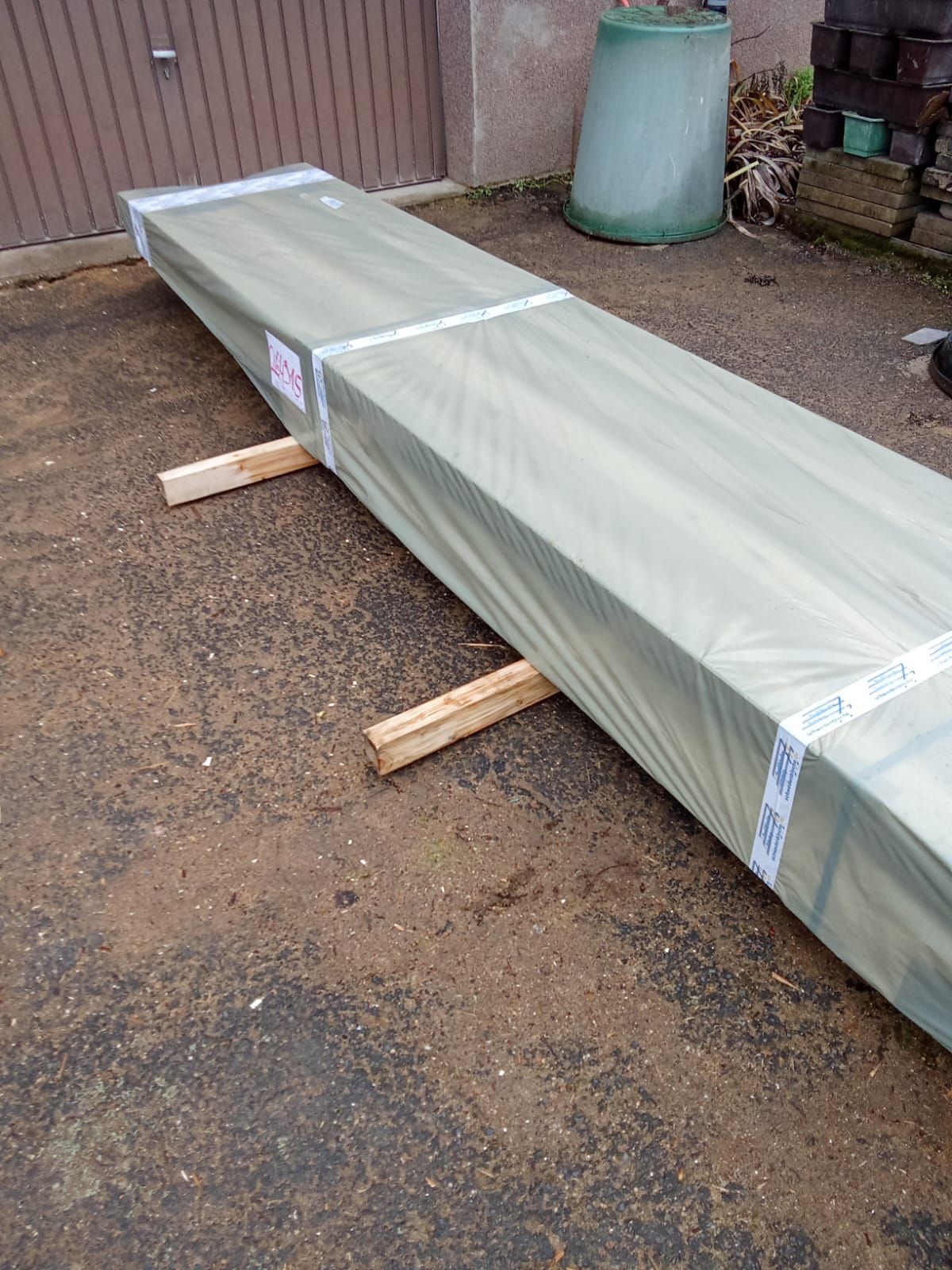 Ein langes, rechteckiges Paket, von Holzklötzen gestützt, vor einem geschlossenen Garagentor.