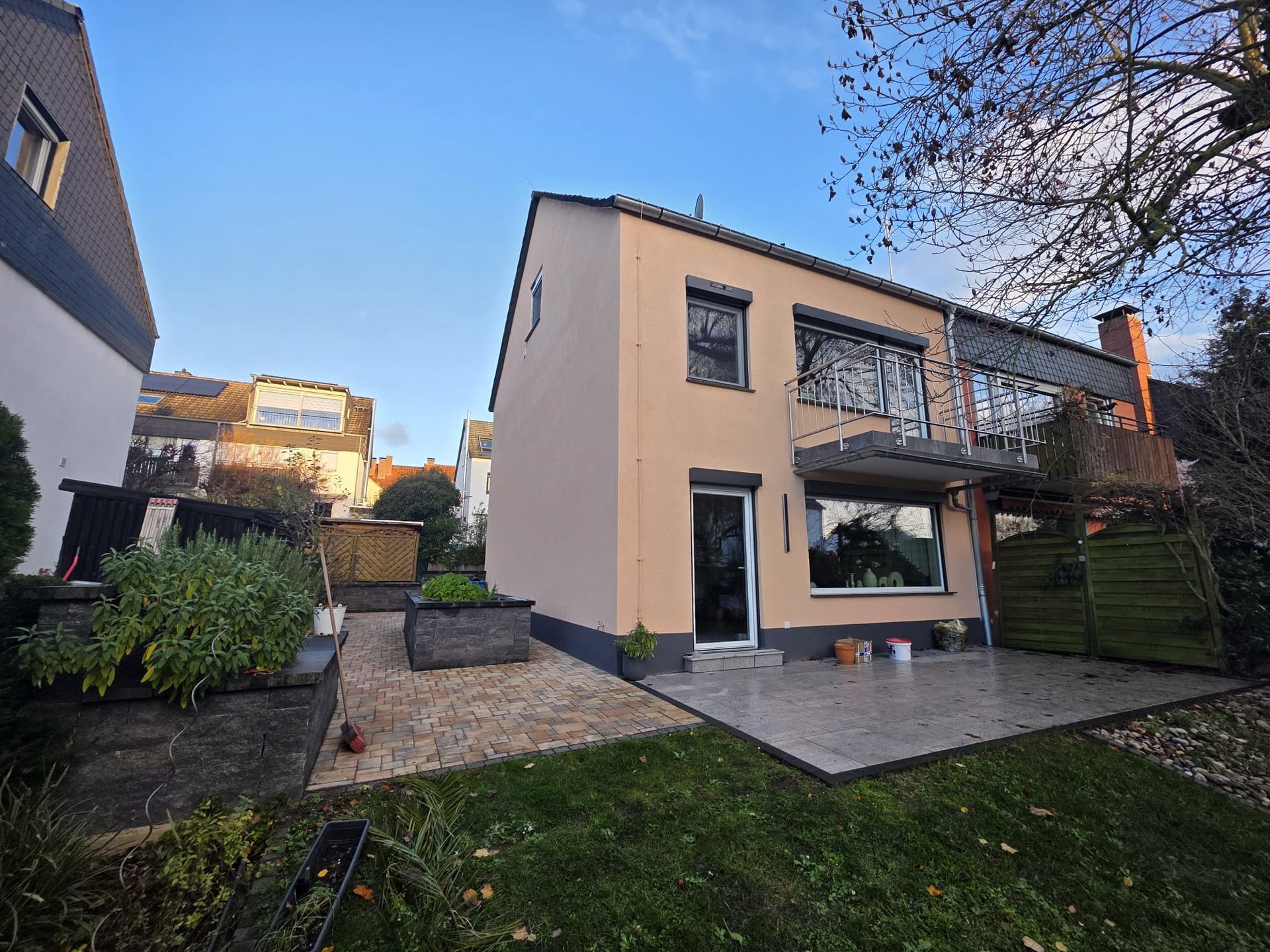 Blick vom Hinterhof eines zweistöckigen Hauses mit hellpfirsichfarbener Fassade, Balkon und Terrasse.