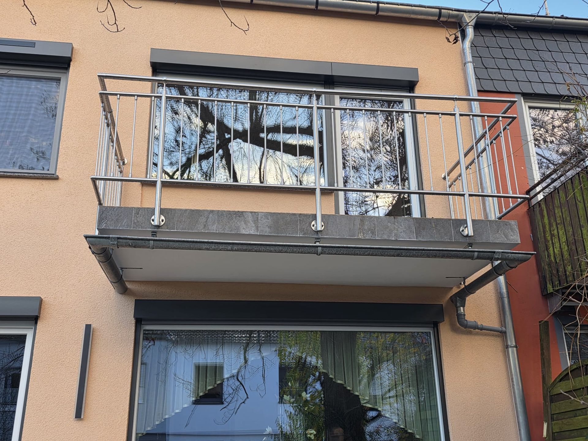 Balkon mit Metallgeländer und Fenster. Gebäudeaußenfassade hellbraun mit Rollläden.