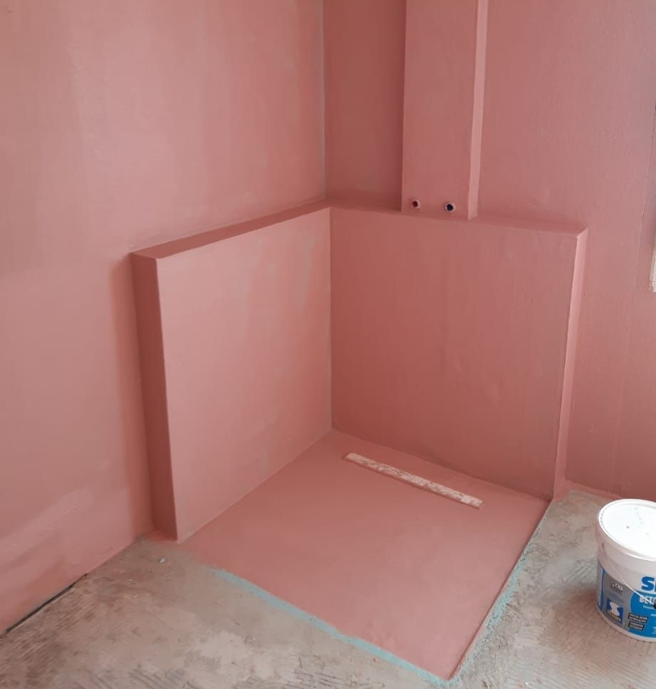 Eine rosa gestrichene Ecke eines Zimmers mit grundierten Wandpaneelen und einem Farbeimer auf dem Boden.