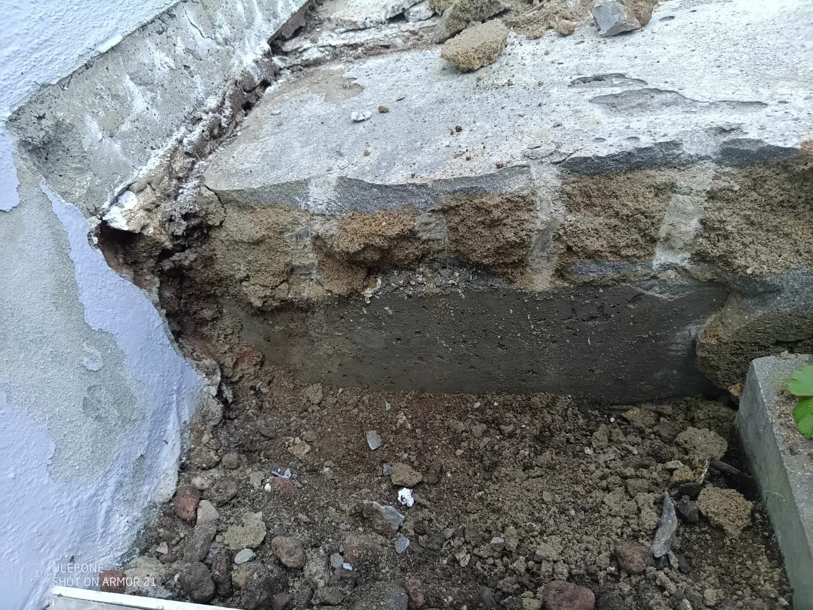 Zerbrochene Betonstufe mit bröckelndem Schmutz und Schutt neben einer Mauer.