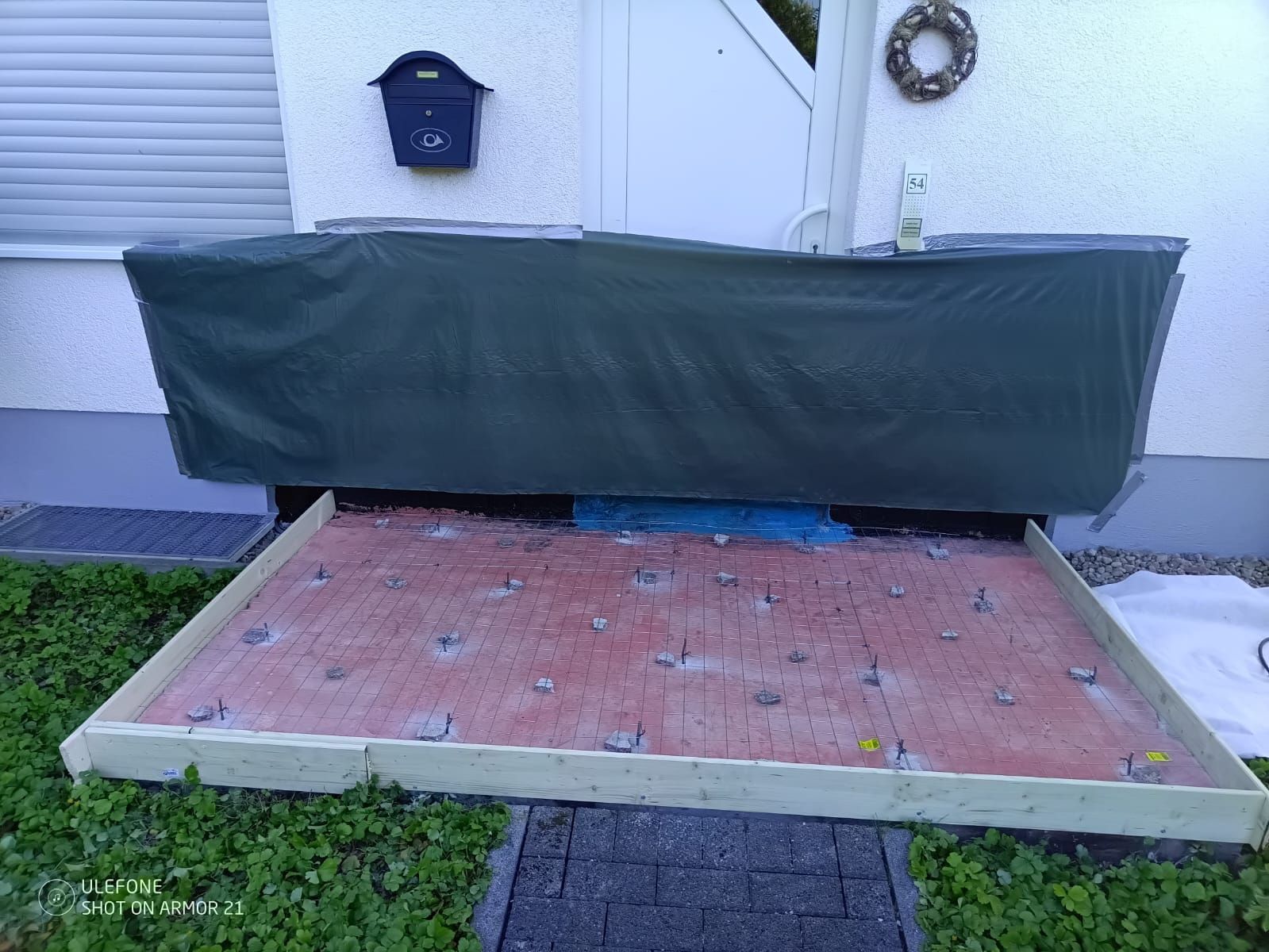 Überdachte Verandatreppe mit einer grünen Plane vor einer weißen Haustür
