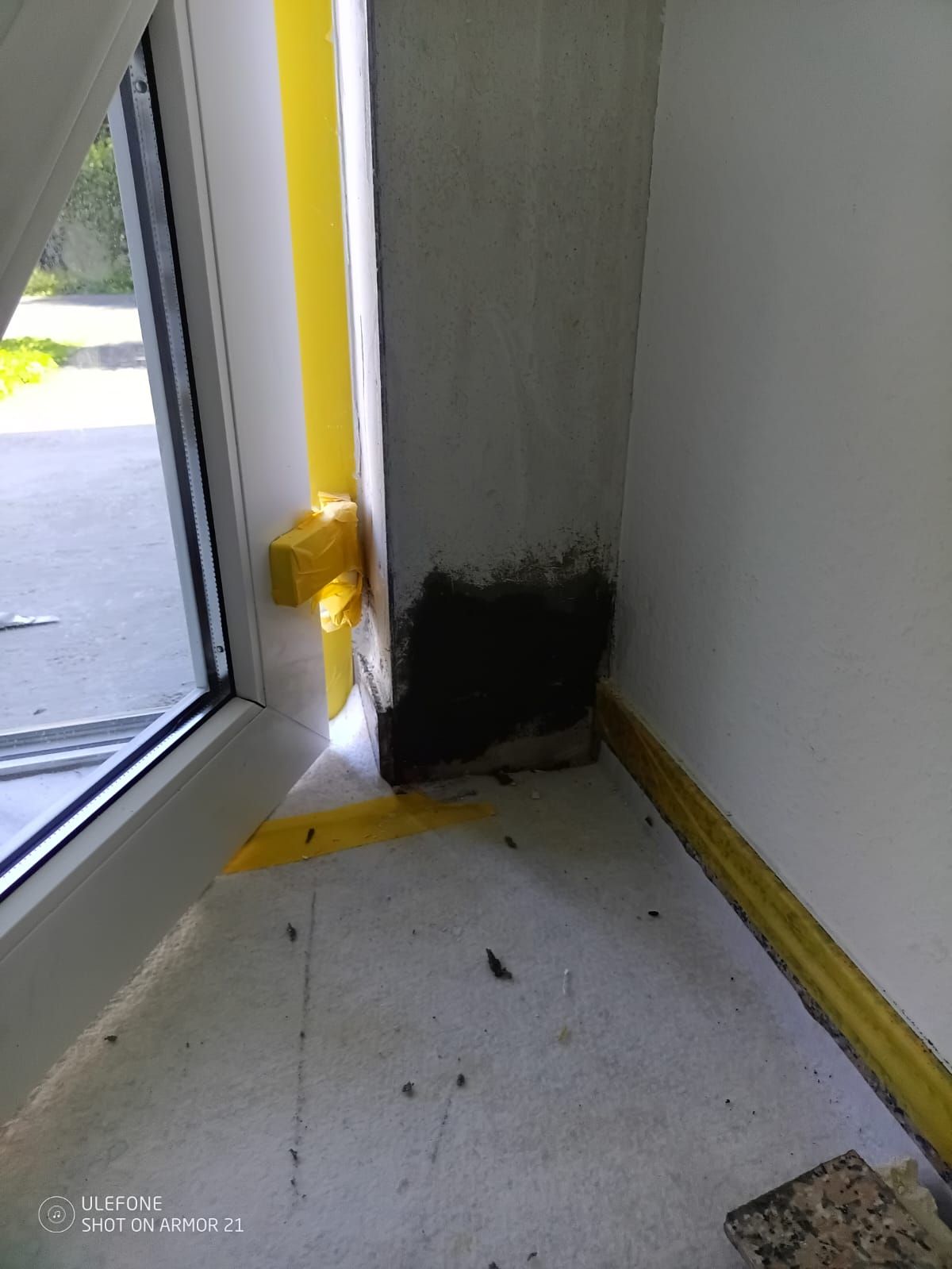Innenecke neben einer Glastür mit dunklem Schimmel oder Rußflecken und gelbem Absperrband.