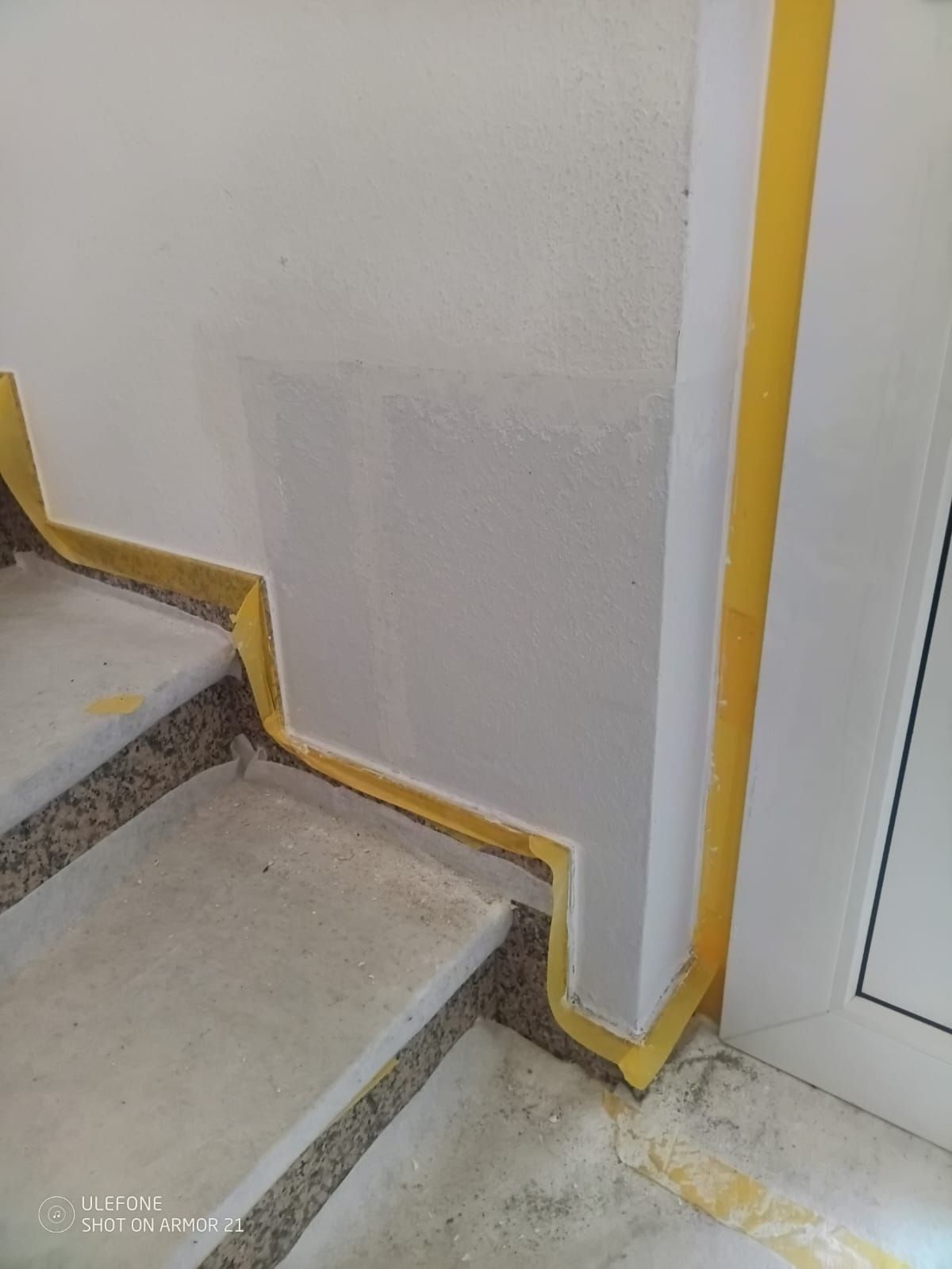 Treppenhausecke mit weißer Wand, gelber Umrandung und zwei grauen Stufen neben einem Türrahmen