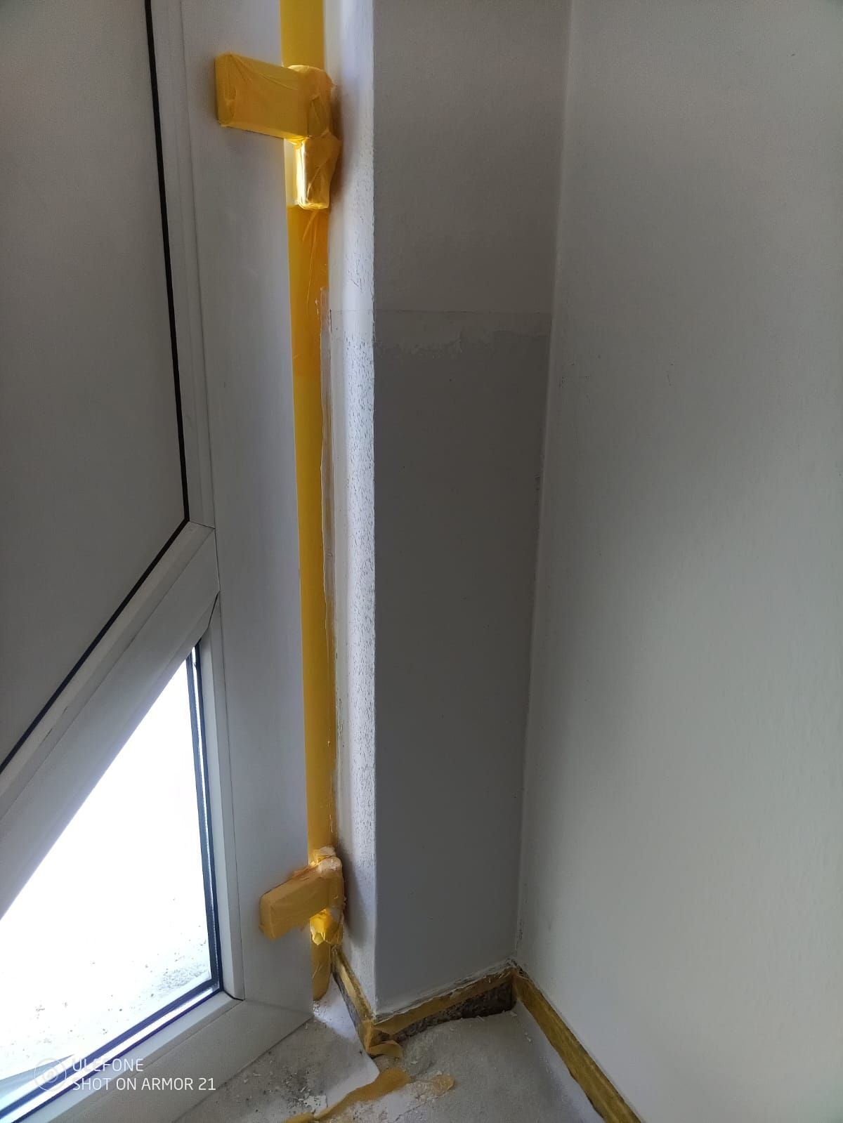 Weiße Eckwand mit gelbem Handlauf und einem kleinen dreieckigen Fenster in Bodennähe.