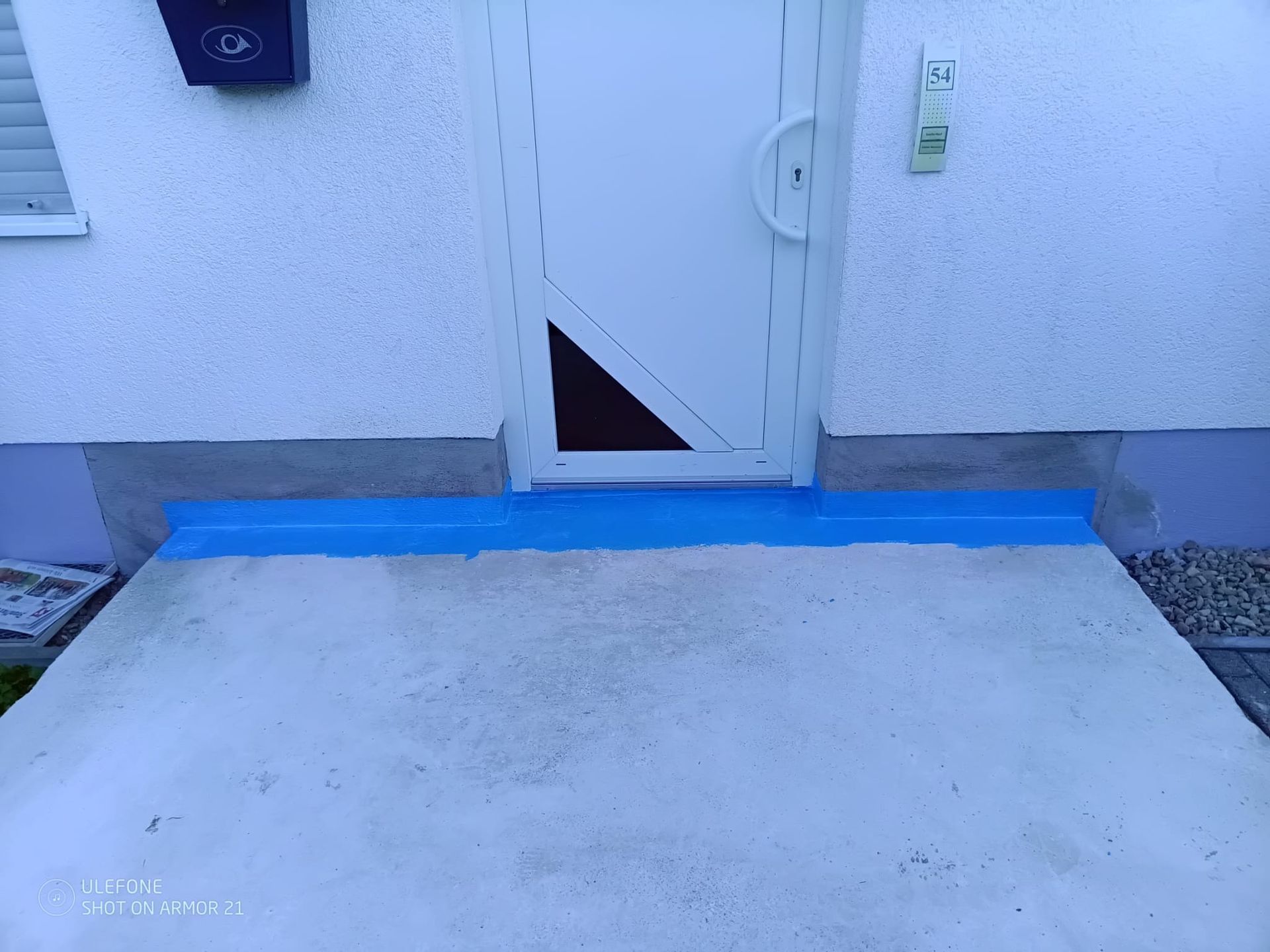 Eine Betonrampe führt zu einer weißen Tür mit blauem Rand an der Schwelle.