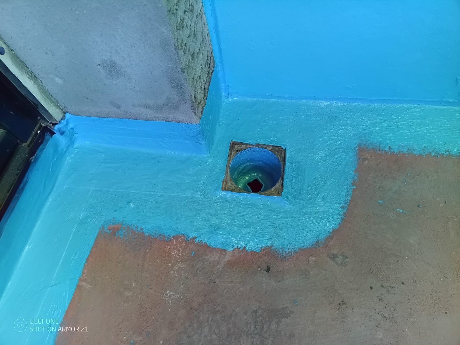 Blauer Boden mit einer kleinen quadratischen Abflussöffnung in der Nähe einer Wand- und Türecke.