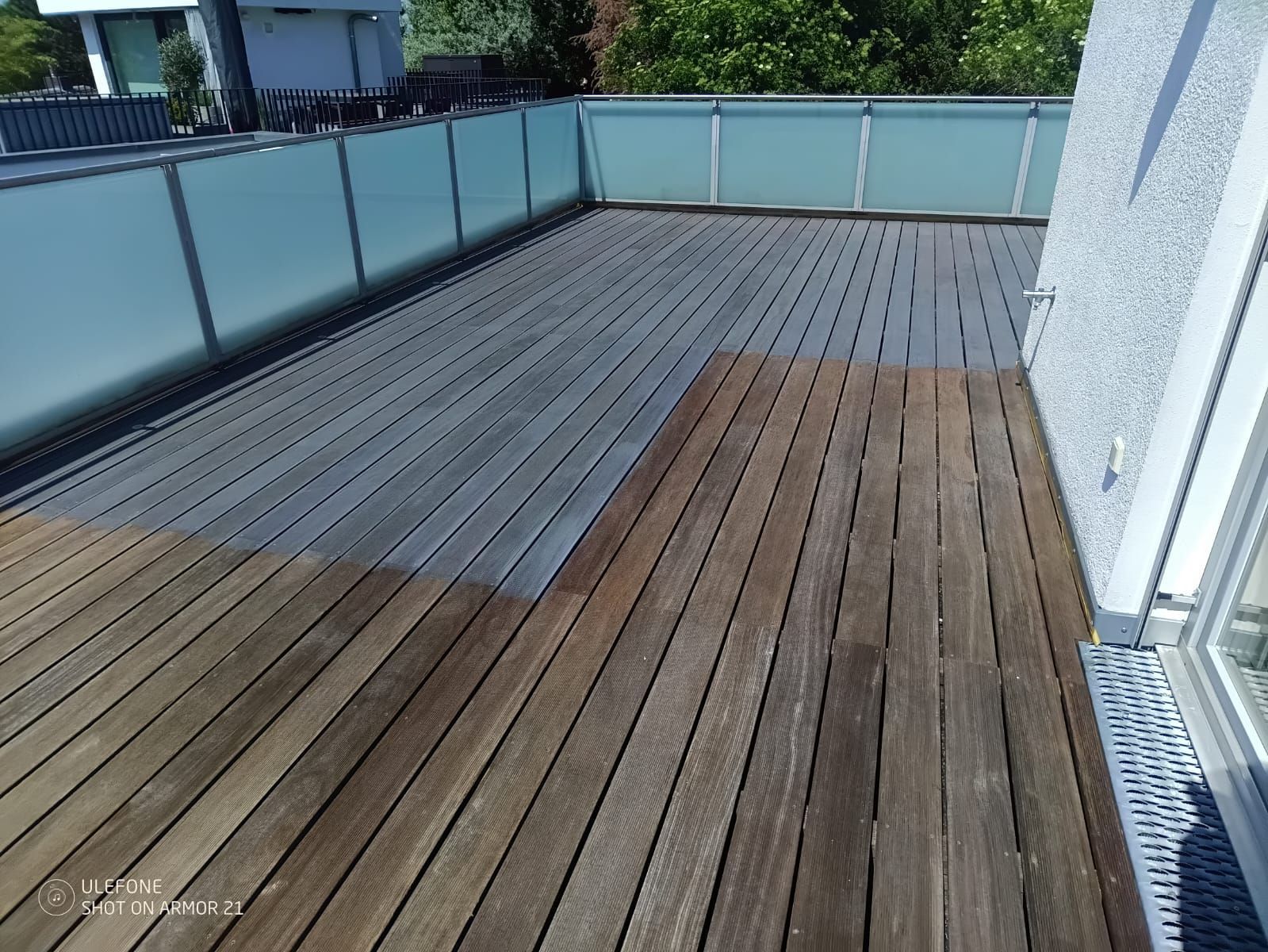 Leere Holzterrasse mit Glasgeländer und blauer Wand, bei Tageslicht betrachtet