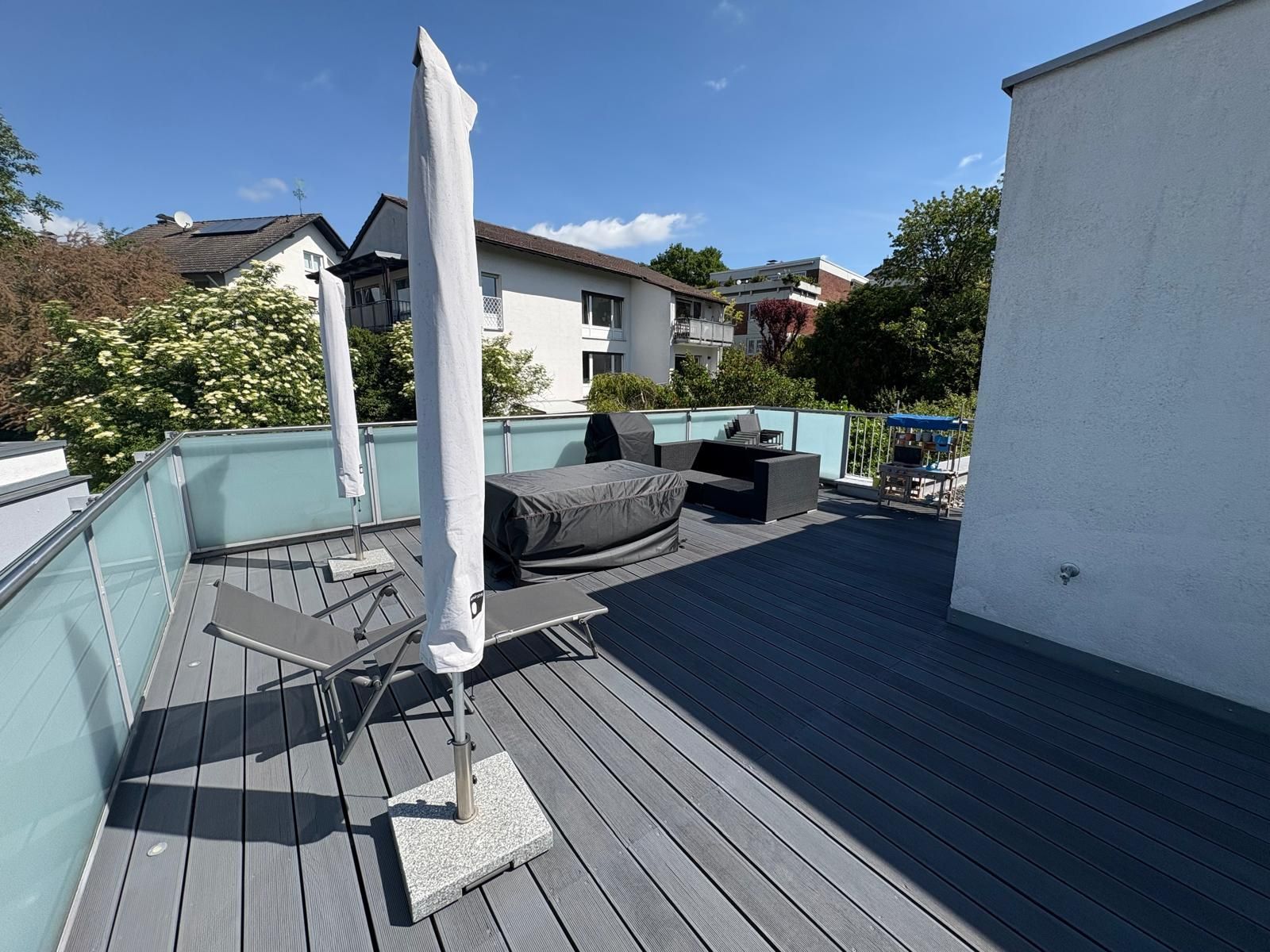 Dachterrasse mit grauem Bodenbelag, Terrassenmöbeln und weißem Sonnensegel unter klarem, blauem Himmel