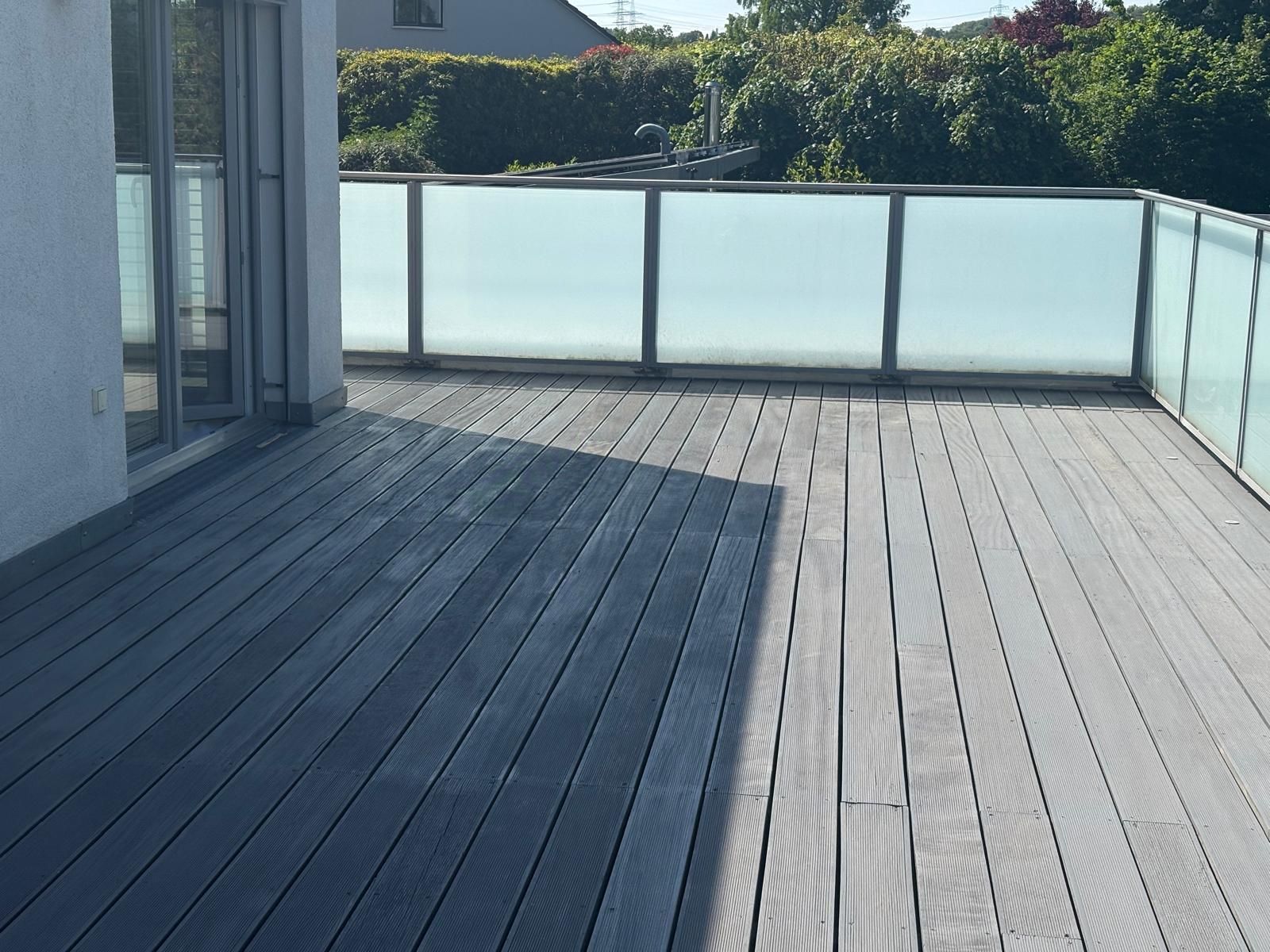 Leere graue Terrasse mit Milchglasgeländer neben einem modernen Haus im Freien