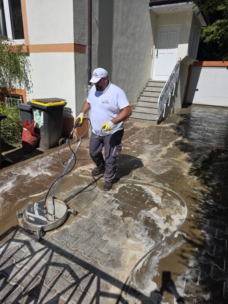 Ein Mann reinigt eine gepflasterte Auffahrt mit einem Flächenreiniger.