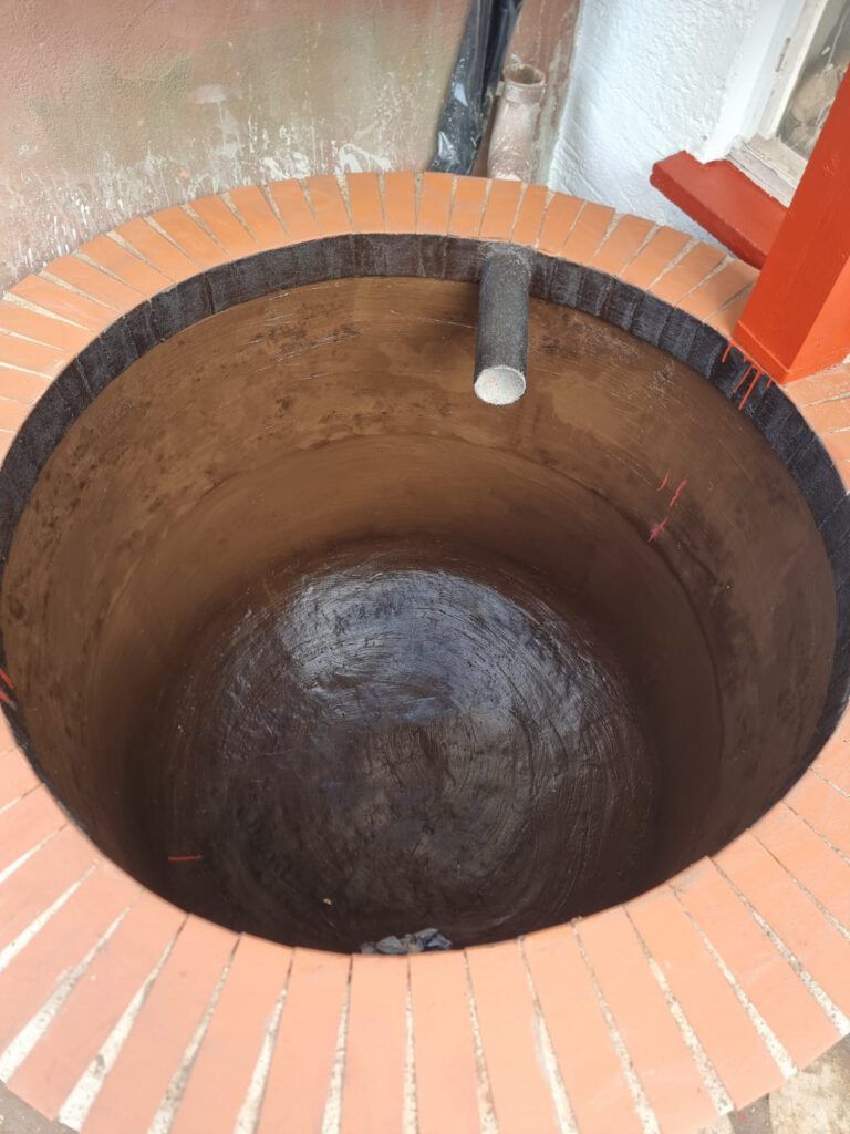 Ein tiefer, runder, mit Ziegeln ausgekleideter Brunnen mit dunklem Innenraum und einem grauen Rohr, das seitlich herausragt.