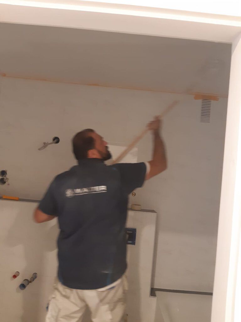 Ein Mann greift in einer Baustelle mit einem Werkzeug an die Decke, um dort Arbeiten durchzuführen.