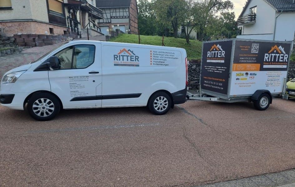 Ein weißer Lieferwagen mit Anhänger, beide mit der Aufschrift „RITTER“, parken vor einem Kundengebäude.