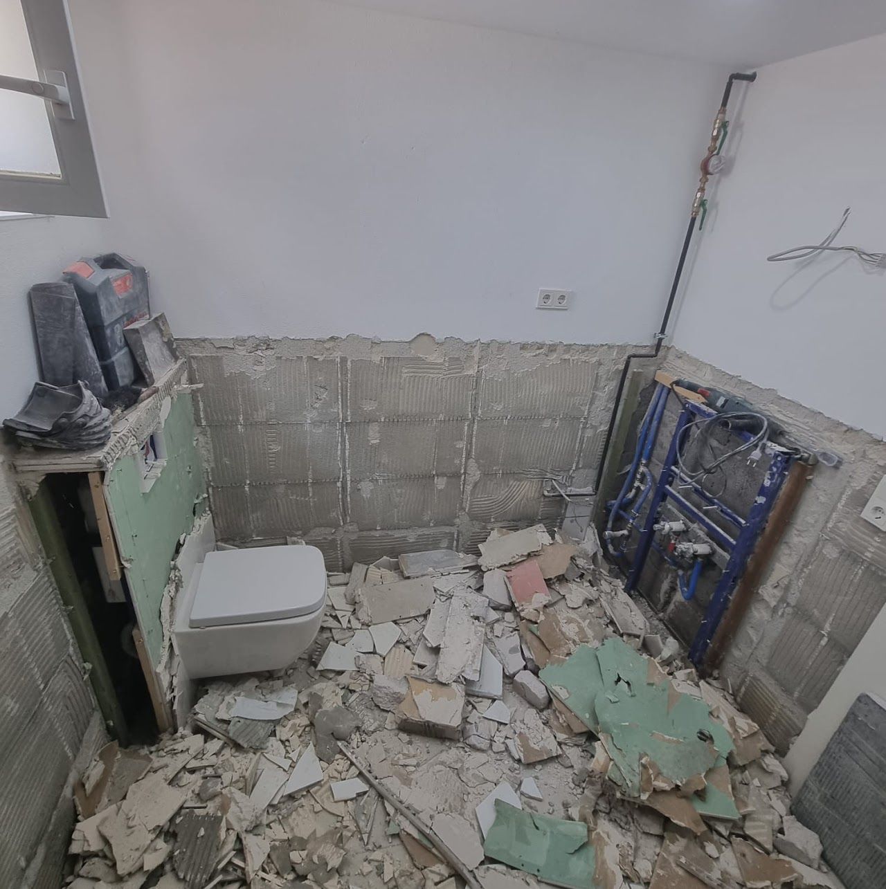 Badezimmer wird renoviert. Toilette installiert, Fliesen von den Wänden entfernt, Bauschutt auf dem Boden.