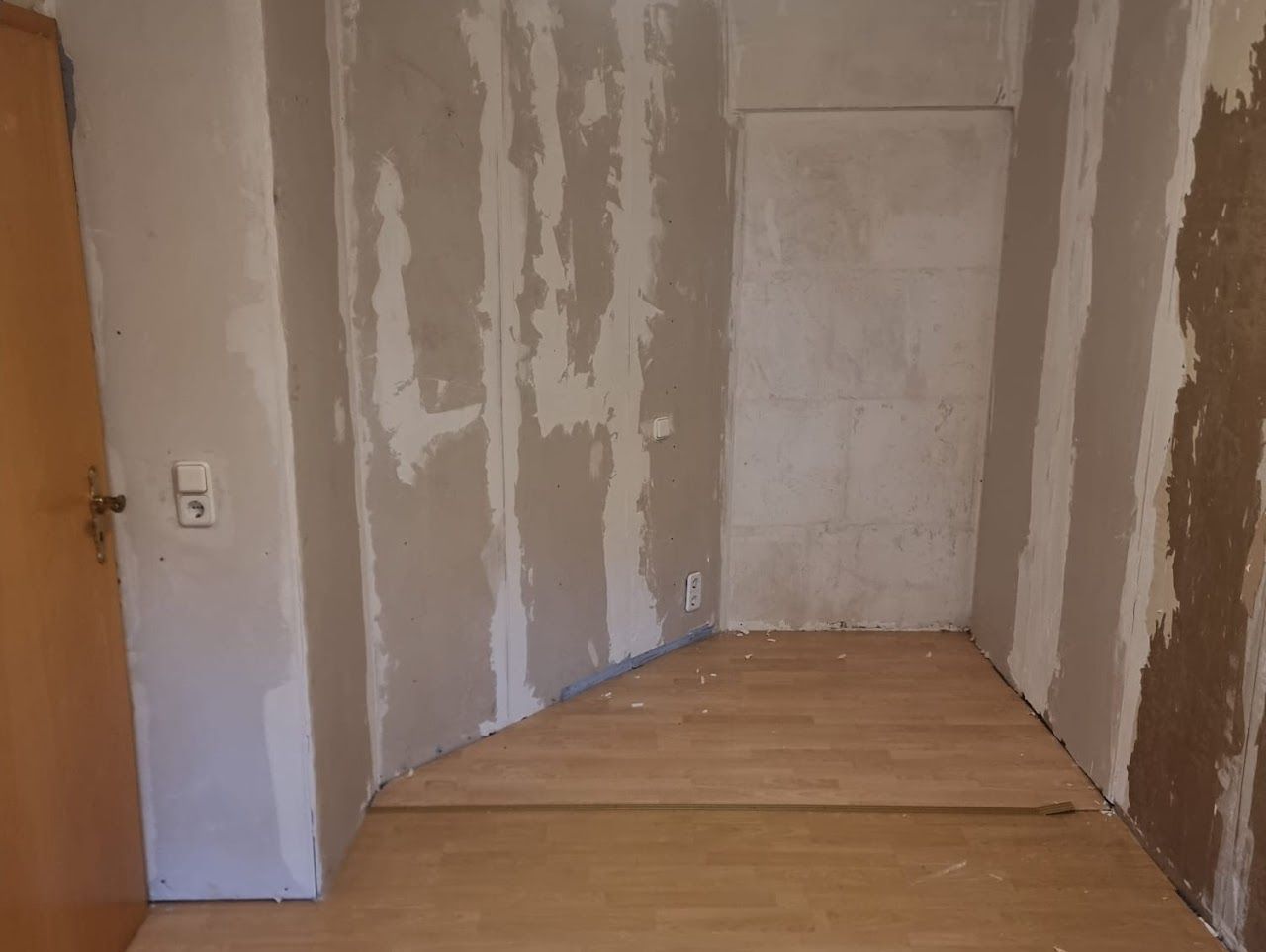 Raum mit unverputzten, teilweise verputzten Wänden. Holzboden mit schrägem Querschnitt.