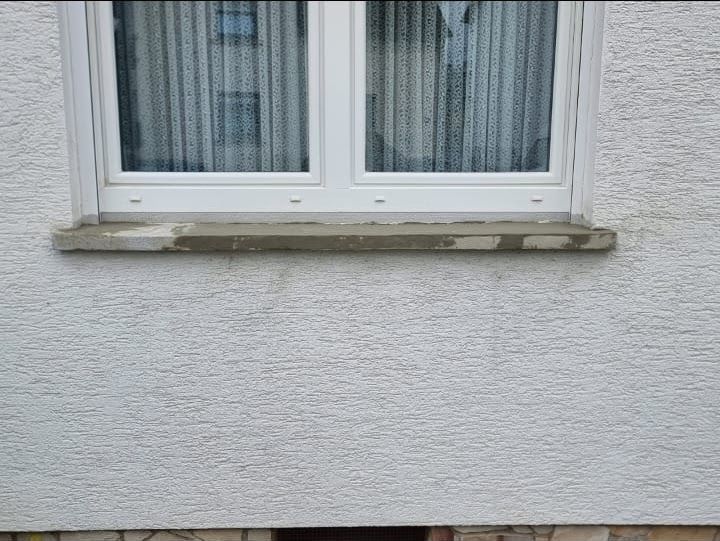 Weißes Fenster mit Betonfensterbank an einer strukturierten weißen Außenwand.