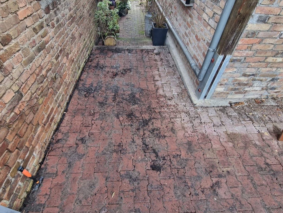 Eine Terrasse aus roten Ziegelsteinen zwischen Ziegelmauern führt zu einem mit Pflanzen bewachsenen Weg.