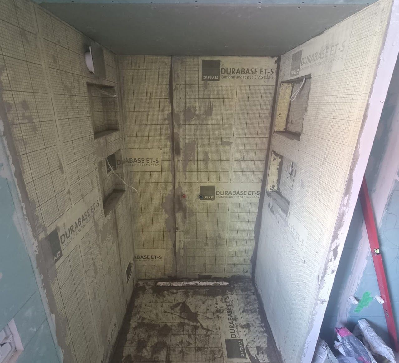 Innenansicht einer im Bau befindlichen Duschkabine; Wände mit wasserdichten Platten verkleidet, kleine Regale.