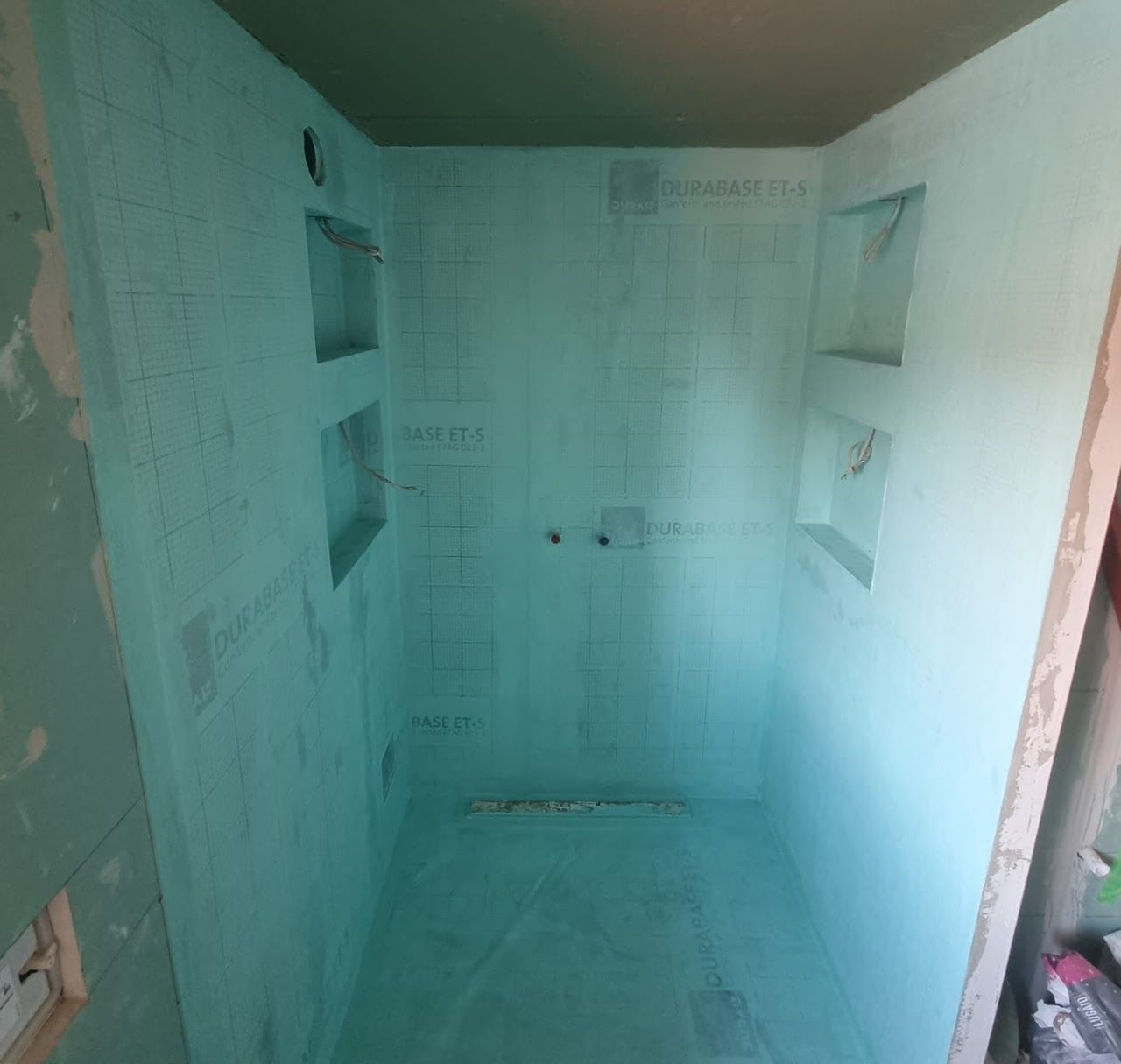 Leere Duschkabine, verkleidet mit türkisfarbenen wasserdichten Platten, mit eingebauten Regalen.