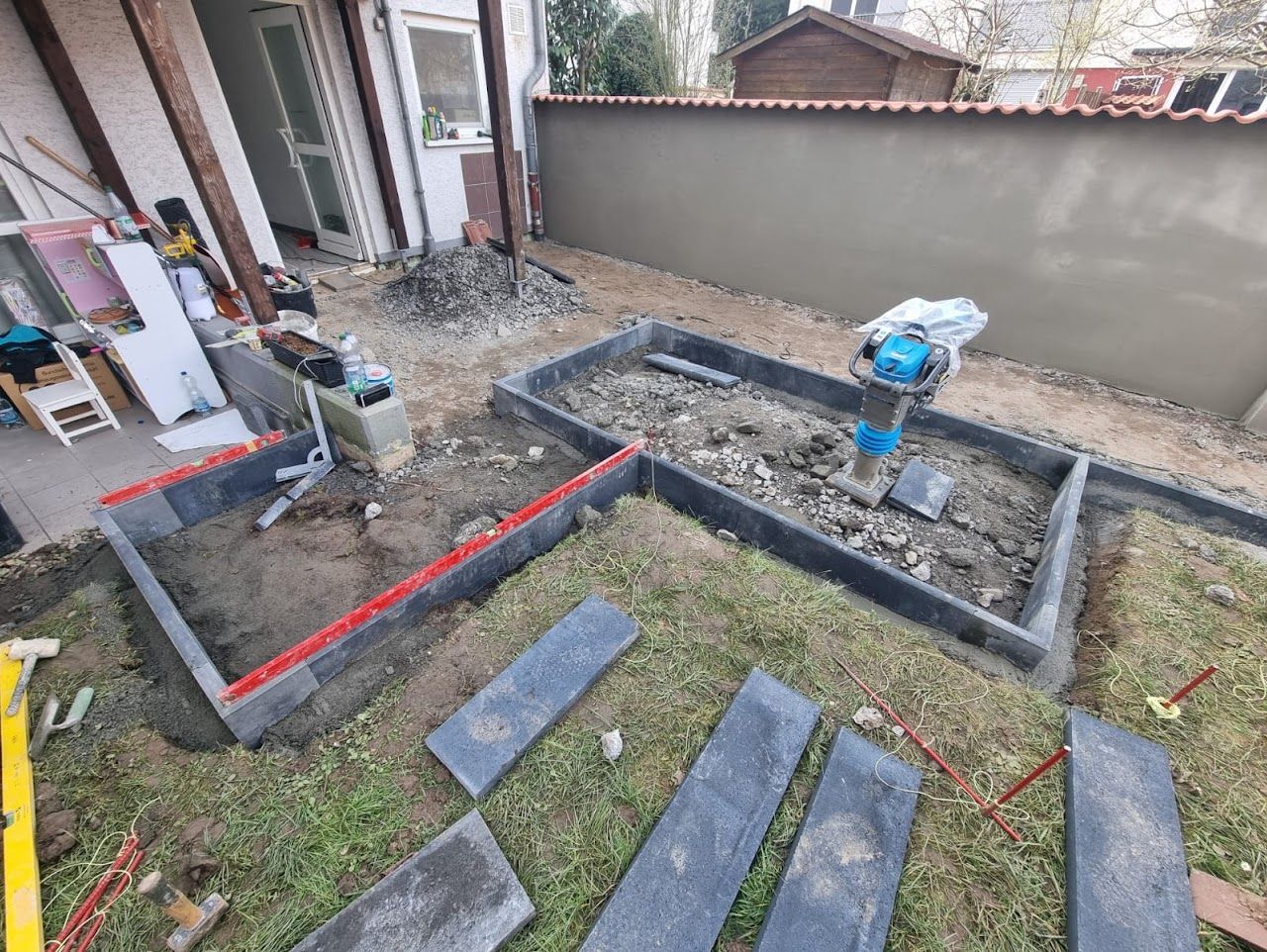 Hinterhof mit zwei im Bau befindlichen rechteckigen Hochbeeten; ein Verdichtungsgerät ist vorhanden.