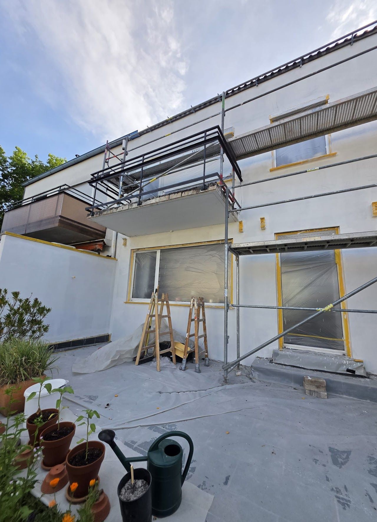 Außenwand eines Gebäudes, das renoviert wird, mit Gerüst, freiliegender Dämmung und sonnigem Himmel.