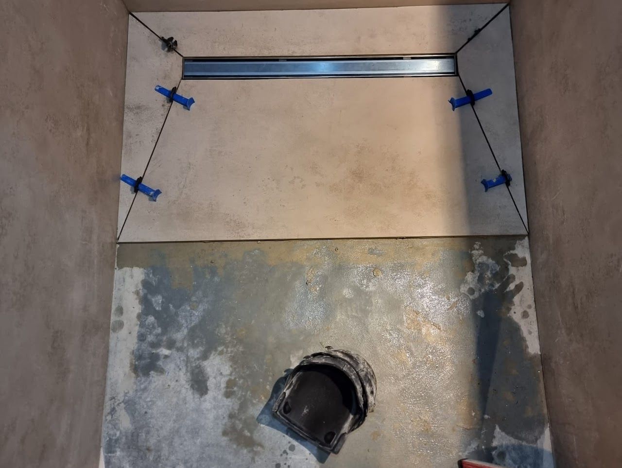 Die Verlegung der Badezimmerbodenfliesen ist im Gange; Linienablauf und Nivellierfüße sind sichtbar.