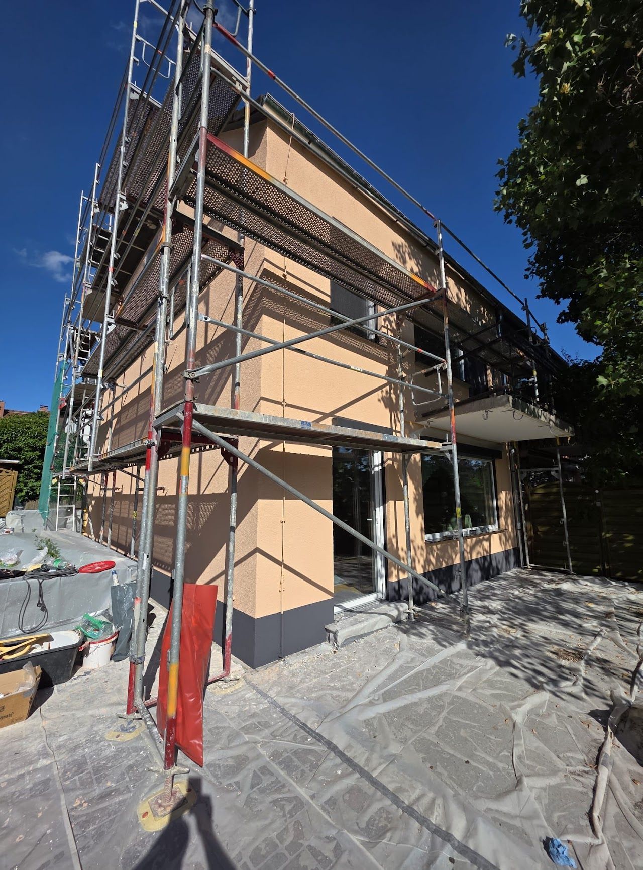Die Fassade eines im Bau befindlichen Gebäudes ist mit Gerüsten versehen, die Wände sind beige, der Himmel klar.