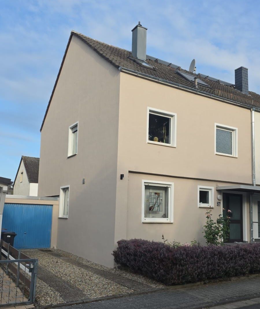 Beiges zweistöckiges Haus mit blauem Garagentor, dunklem Dach und kleinem Vorgarten.