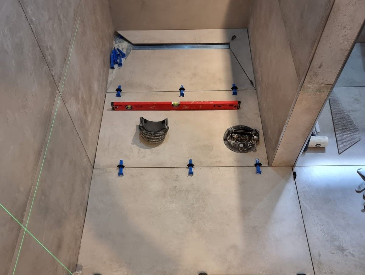 Badezimmer im Bau mit Fliesen, Wasserwaage, Abfluss und blauen Nivellierklammern.