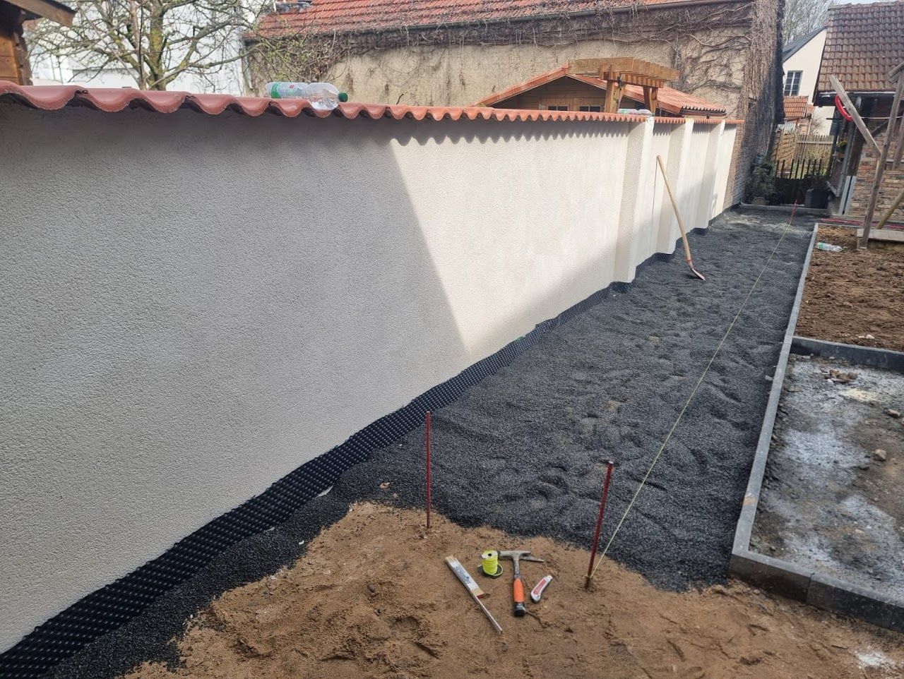 Ein im Bau befindlicher Schotterweg verläuft neben einer Stuckwand mit rotem Ziegeldach.