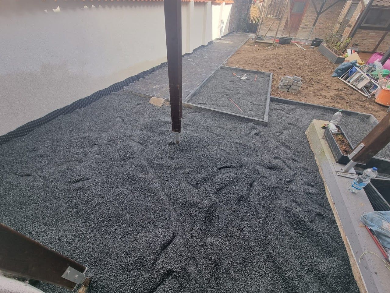 Kiesboden als teilweiser Belag auf einer Terrasse, in der Nähe einer weißen Mauer und einer Holzkonstruktion.