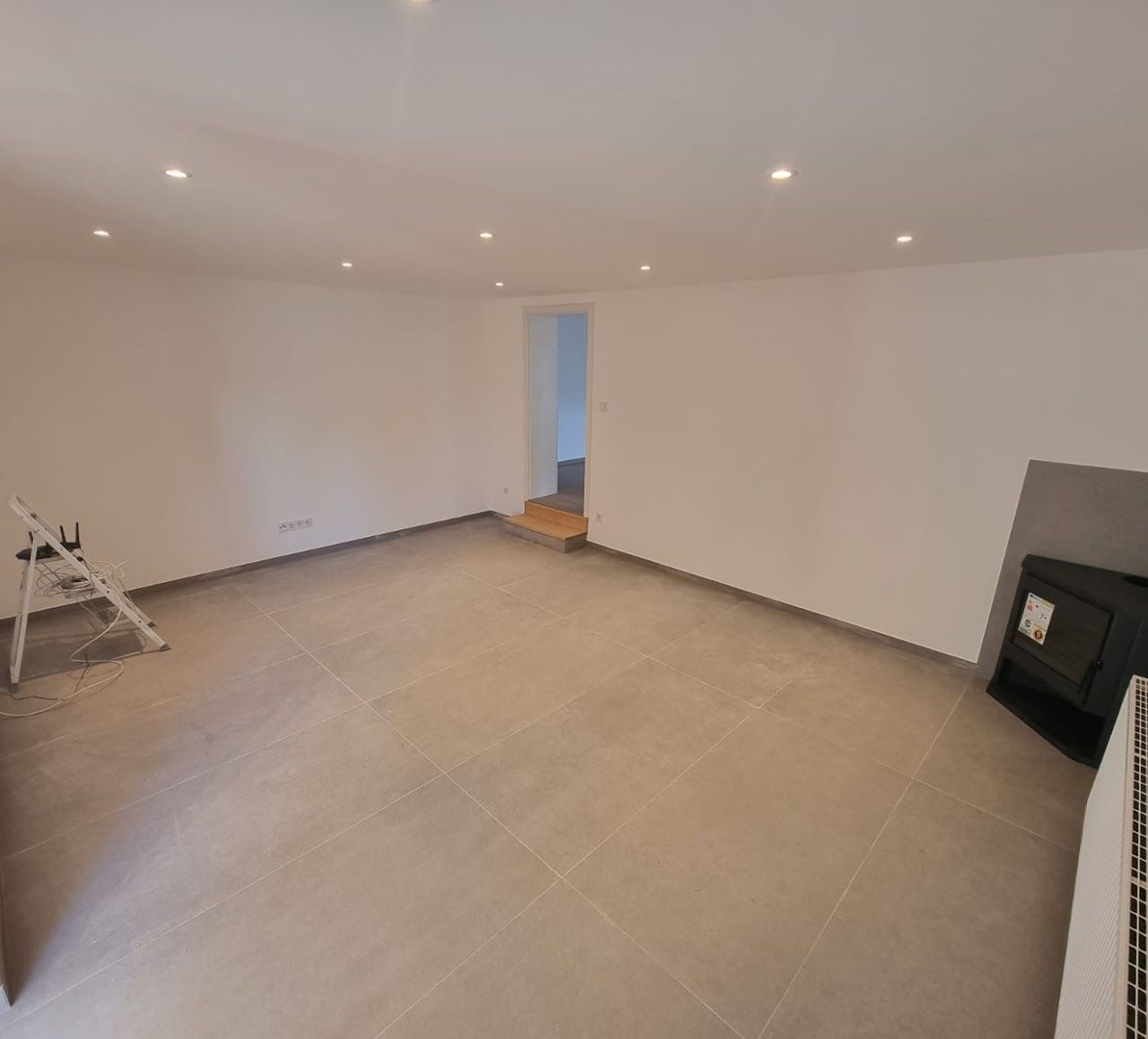 Leeres, frisch gestrichenes Zimmer mit grauen Fliesenböden, Einbaustrahlern und einem kleinen Türrahmen.