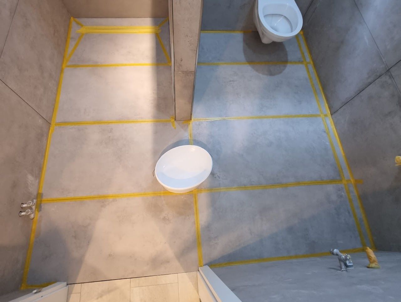 Badezimmerboden mit gelbem Klebeband in Gitterstruktur, Toilette sichtbar.