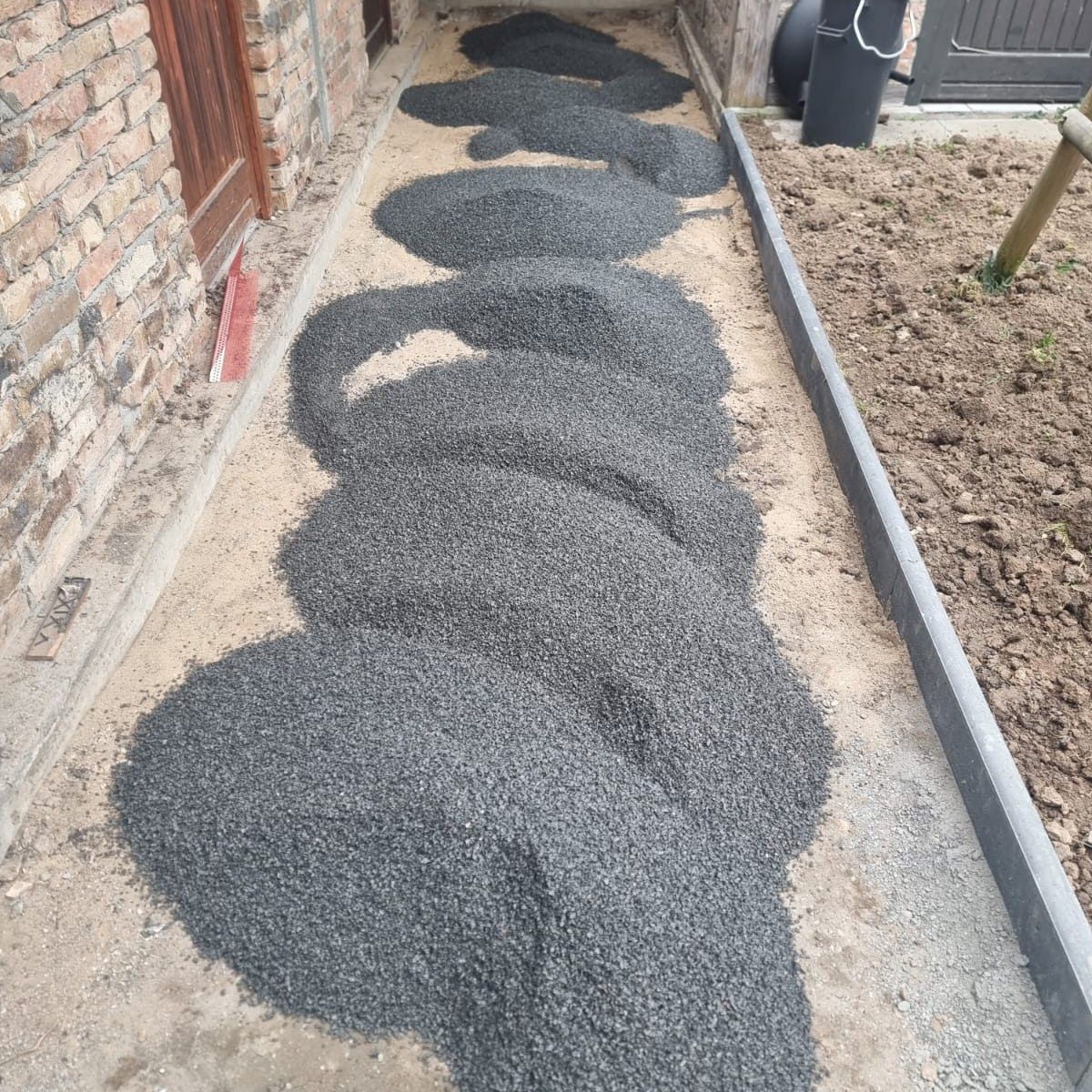 Kieshaufen auf einem Betonweg neben einem Gebäude, wahrscheinlich für die Landschaftsgestaltung.