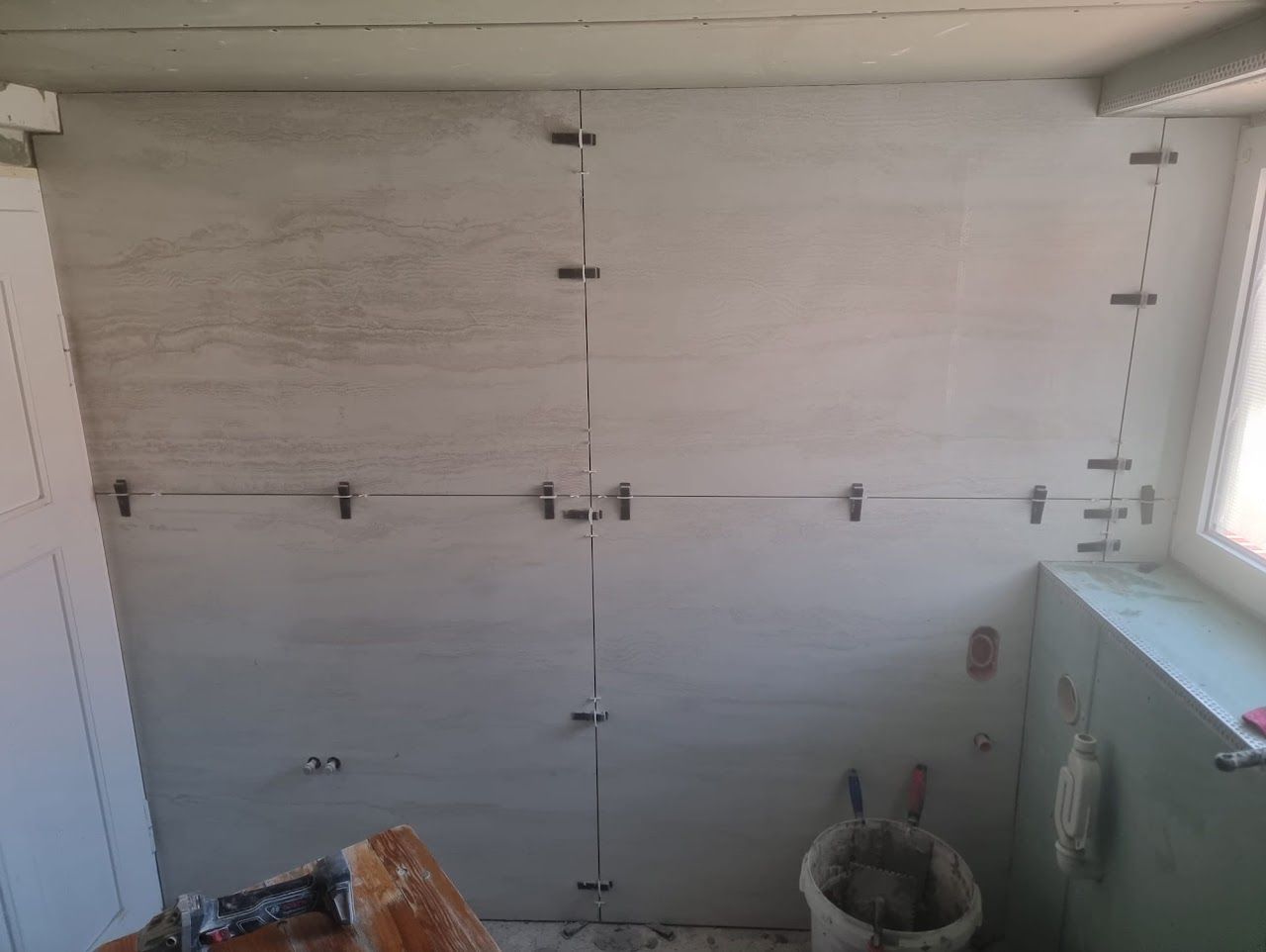 Fliesen werden mit Abstandshaltern an einer Wand verlegt. Innenraum, neutrale Farben.