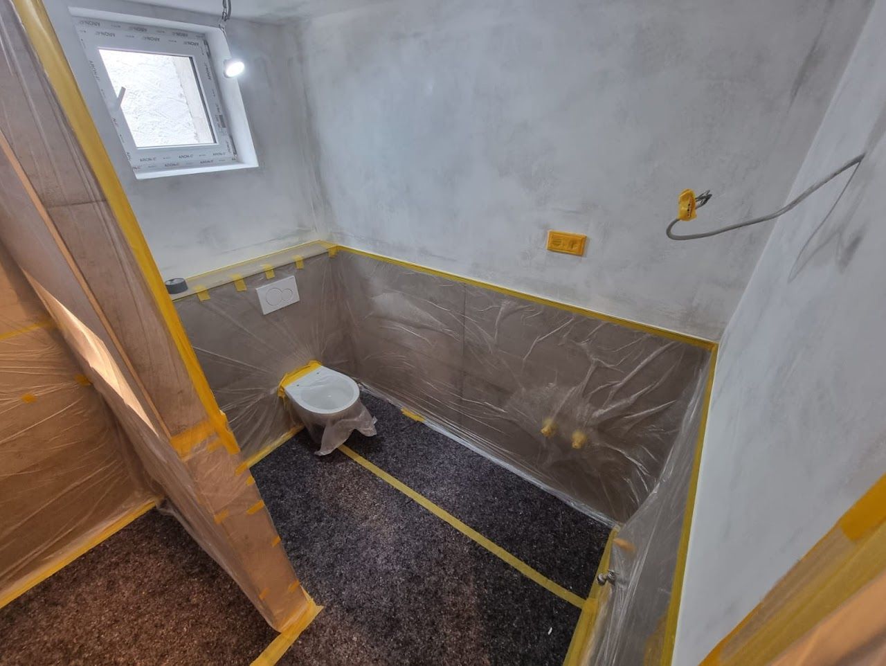 Badezimmer im Umbau, mit Toilette, mit Plastikfolie verkleideten Wänden und Schutzband.