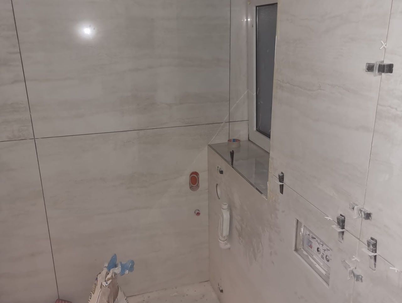 Badezimmer mit weißen Marmorfliesen, Fenster und Sanitärarmaturen. Teilweise gefliest.