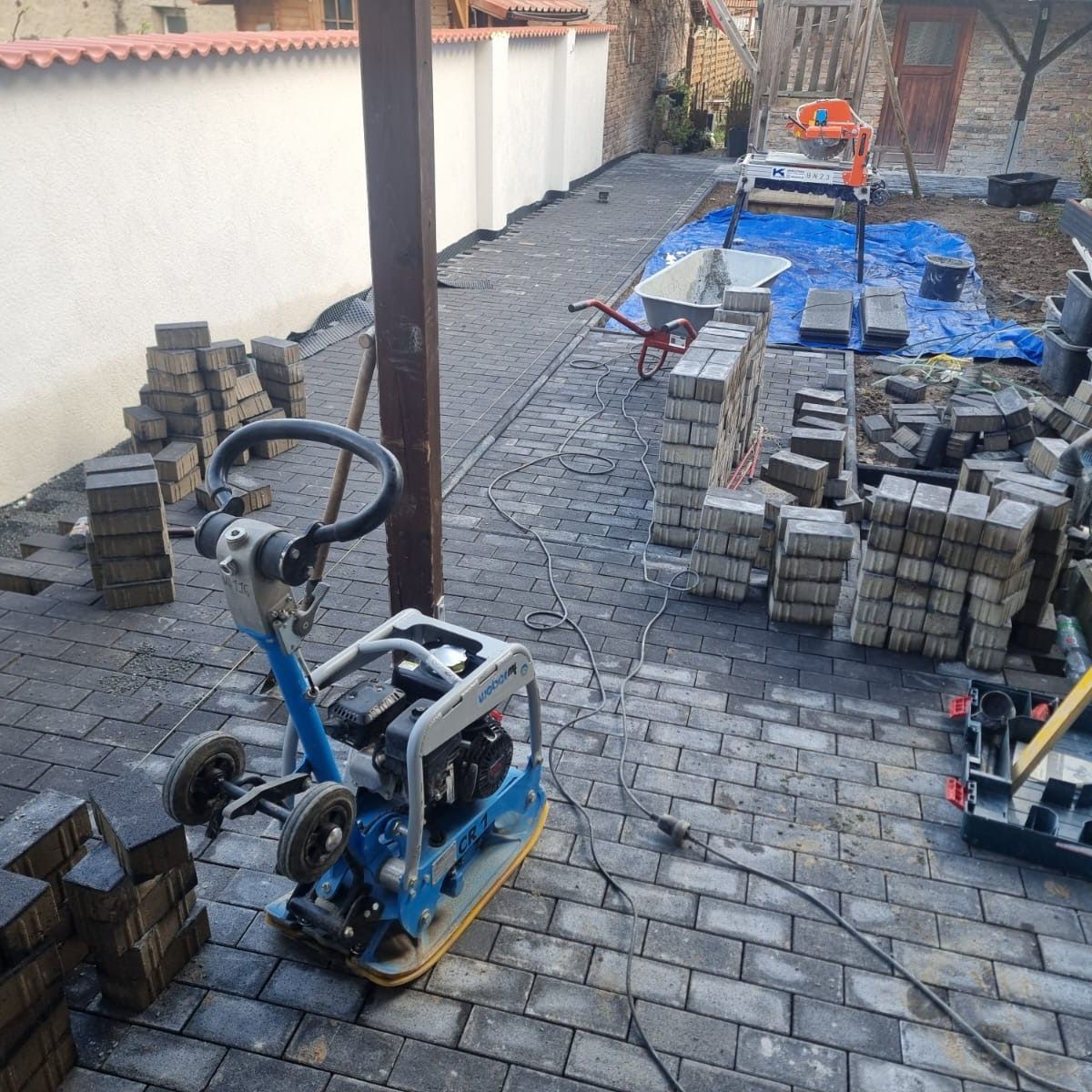 Baustelle mit Pflasterarbeiten; eine Rüttelplatte und gestapelte Pflastersteine.