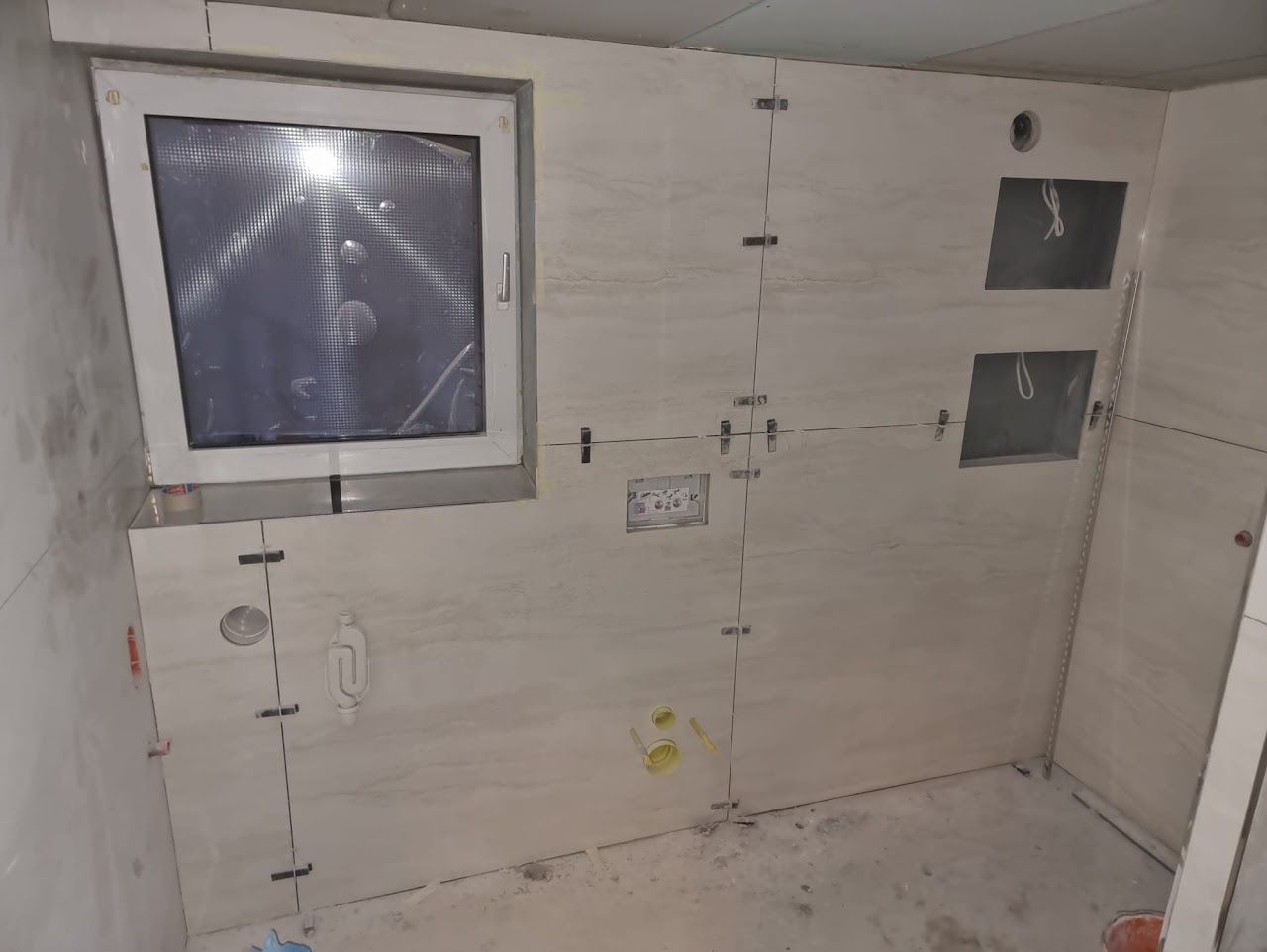 Die Badezimmerwand befindet sich im Bau, ist gefliest und mit Fenstern, Elektroöffnungen und Fliesenabstandshaltern versehen.