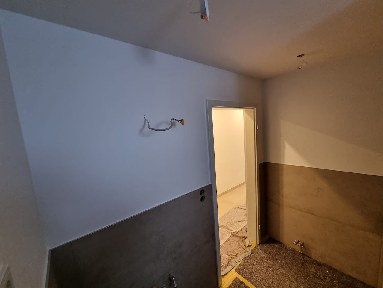 Flur mit weiß-grauen Wänden, Türöffnung und unfertigem Fußboden.