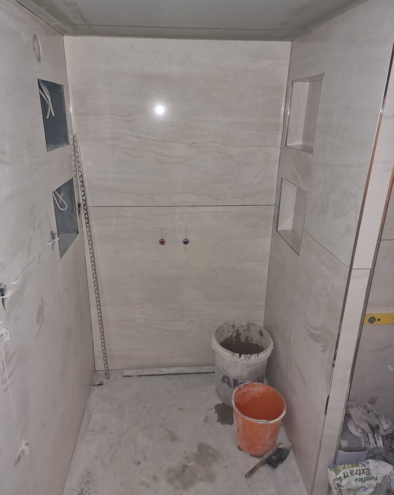 Die Badezimmersanierung ist im Gange, die Wände sind gefliest, inklusive Einbauschränken und Sanitärarmaturen.