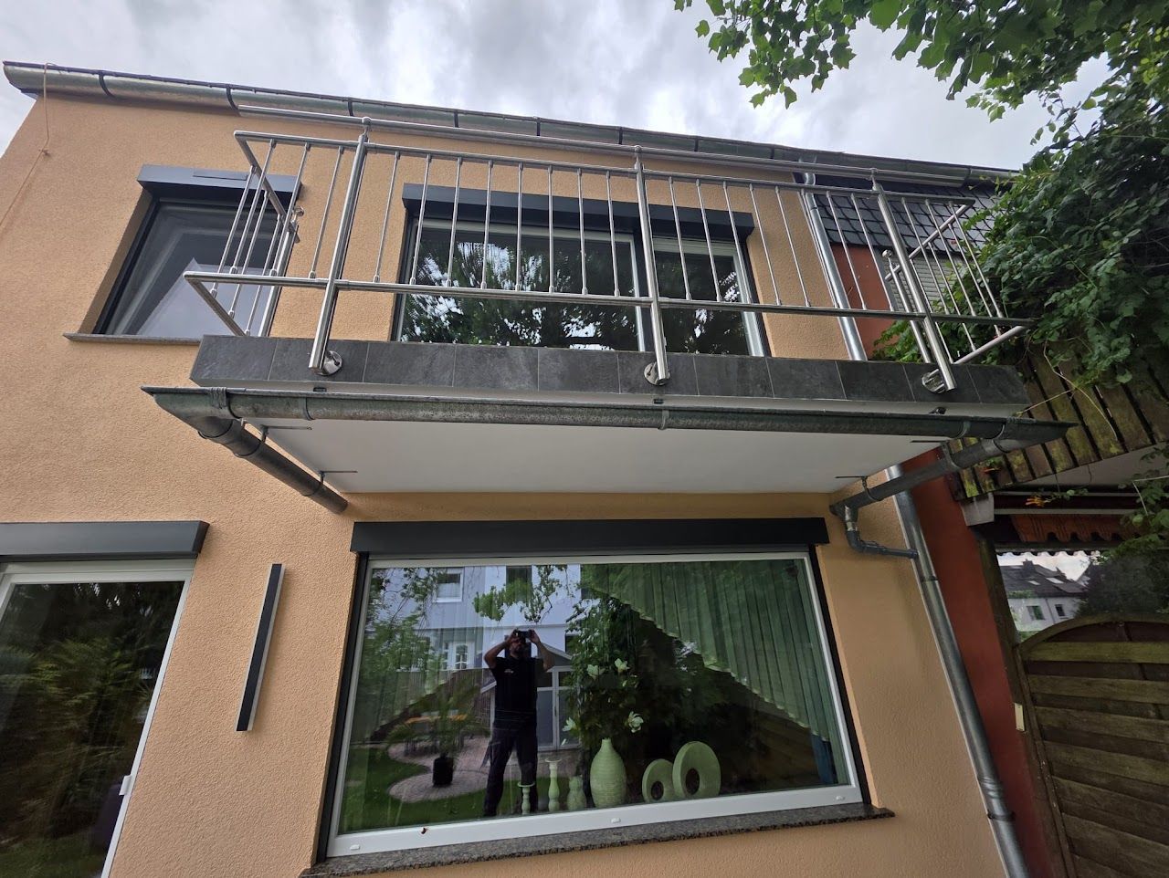 Zweistöckiges Gebäude mit Balkon, Metallgitter an den Fenstern. Spiegelnde Fenster, bedeckter Himmel.