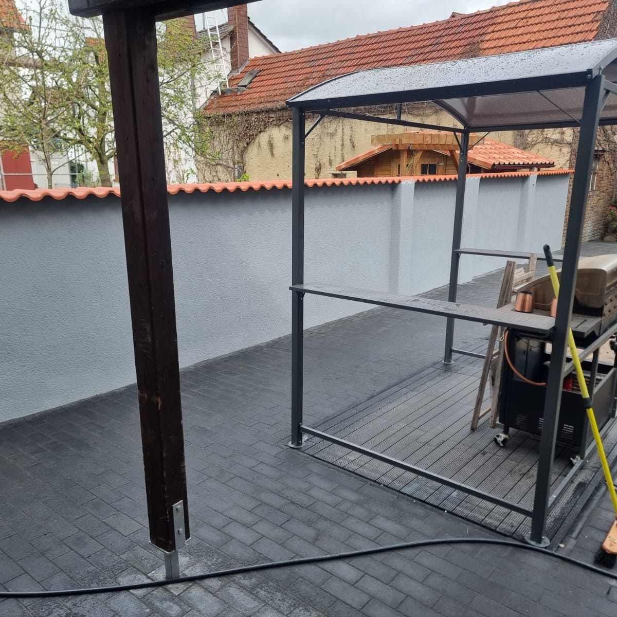 Terrasse im Freien mit Pavillon, Ziegelboden und grauer Wand.