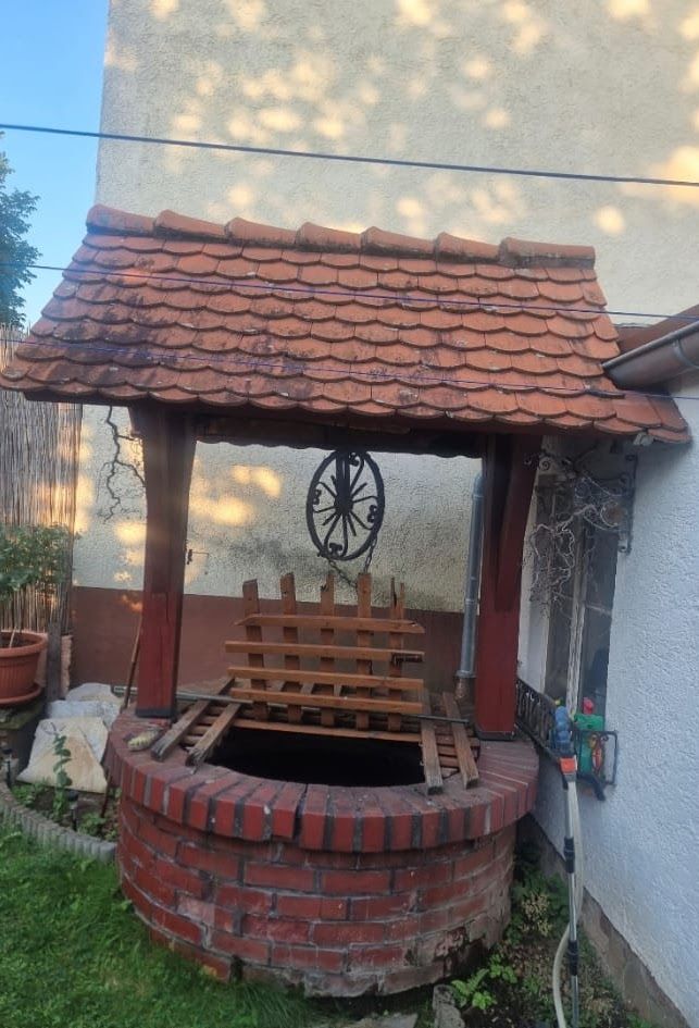Ein Brunnen aus rotem Backstein mit Holzdach und einem dekorativen Rad.